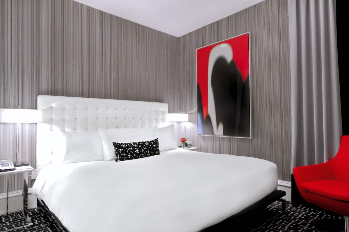 A modern hotel room with a large bed, a red chair, and a large abstract painting on the wall.
