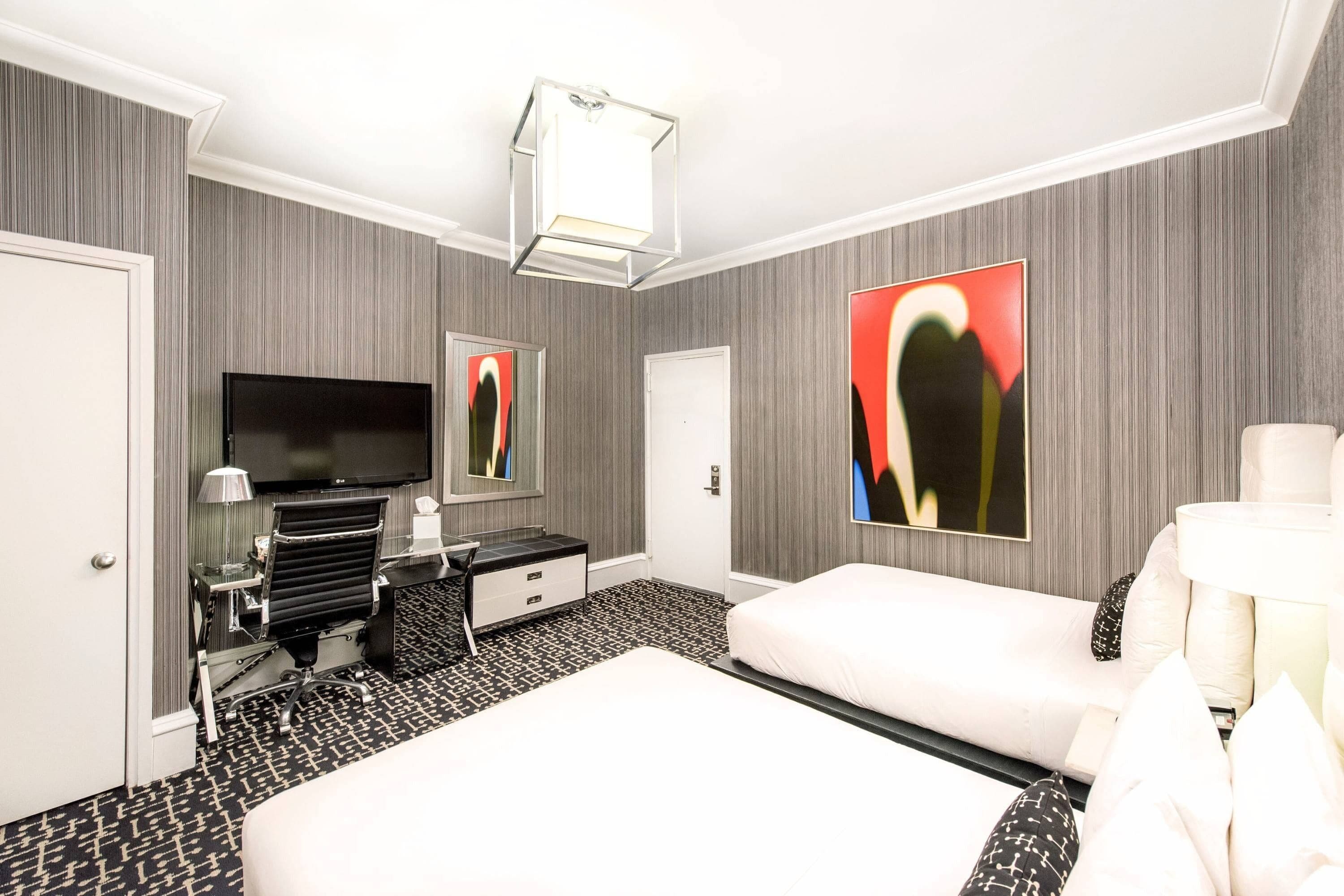 A hotel room with a large bed, a desk with a chair, a flat-screen TV, and artwork on the walls.