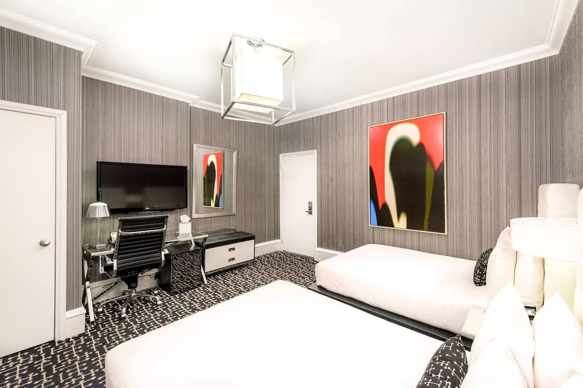 Quarto de hotel com uma cama grande, uma escrivaninha com cadeira, televisão de tela plana e obras de arte nas paredes.