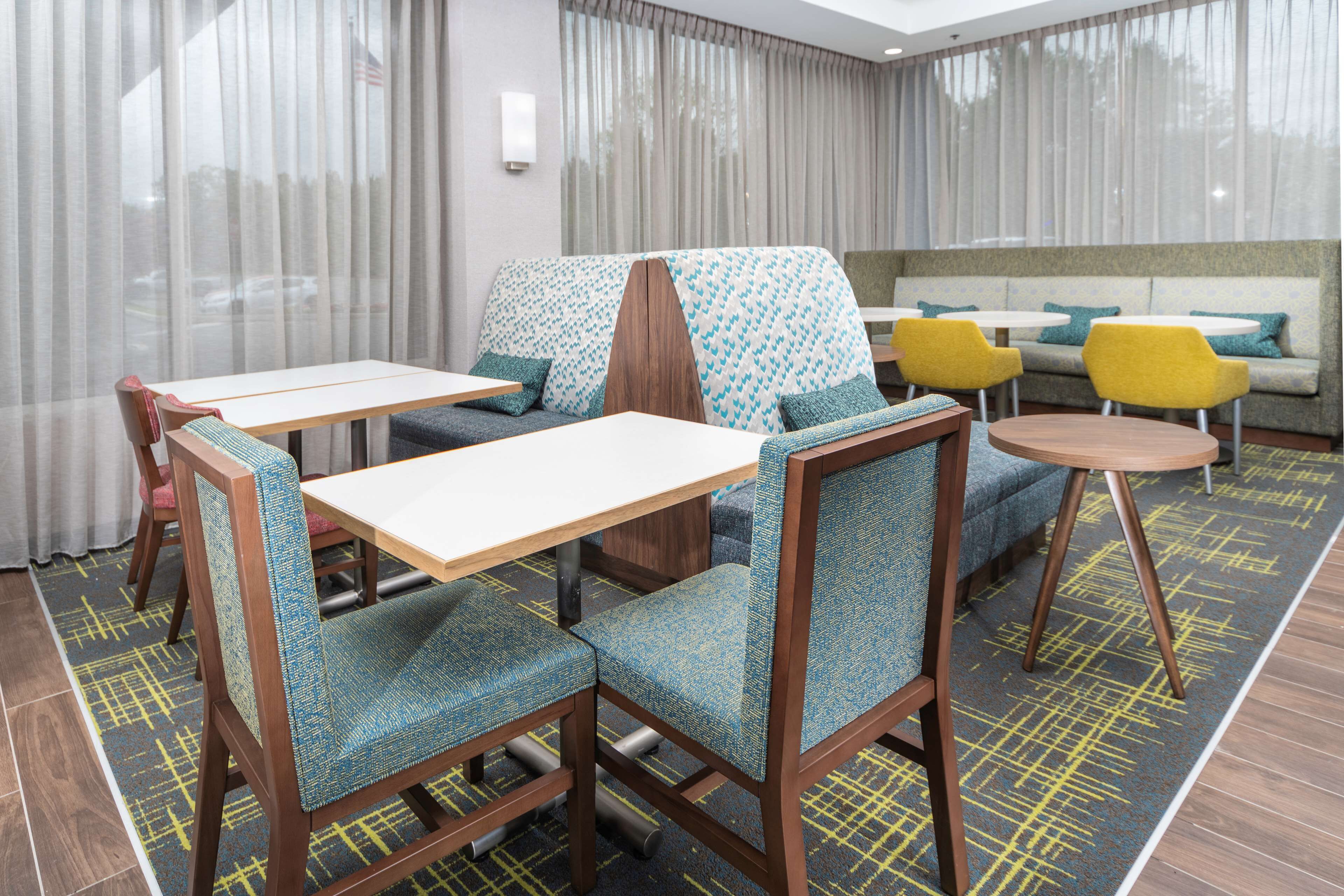 A hotel room with a dining area featuring wooden chairs and tables, a sofa, and a patterned rug.