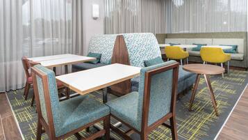 A hotel room with a dining area featuring wooden chairs and tables, a sofa, and a patterned rug.