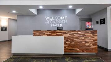 Un mostrador de recepción con un cartel que dice "Welcome to the Garden State", una pared de madera y una alfombra con estampado negro y amarillo.