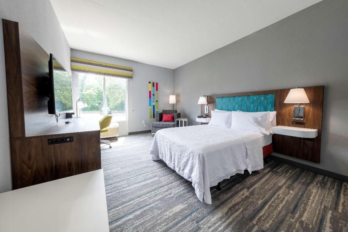 A hotel room with a bed, bedside tables, a TV, a desk, and a chair.