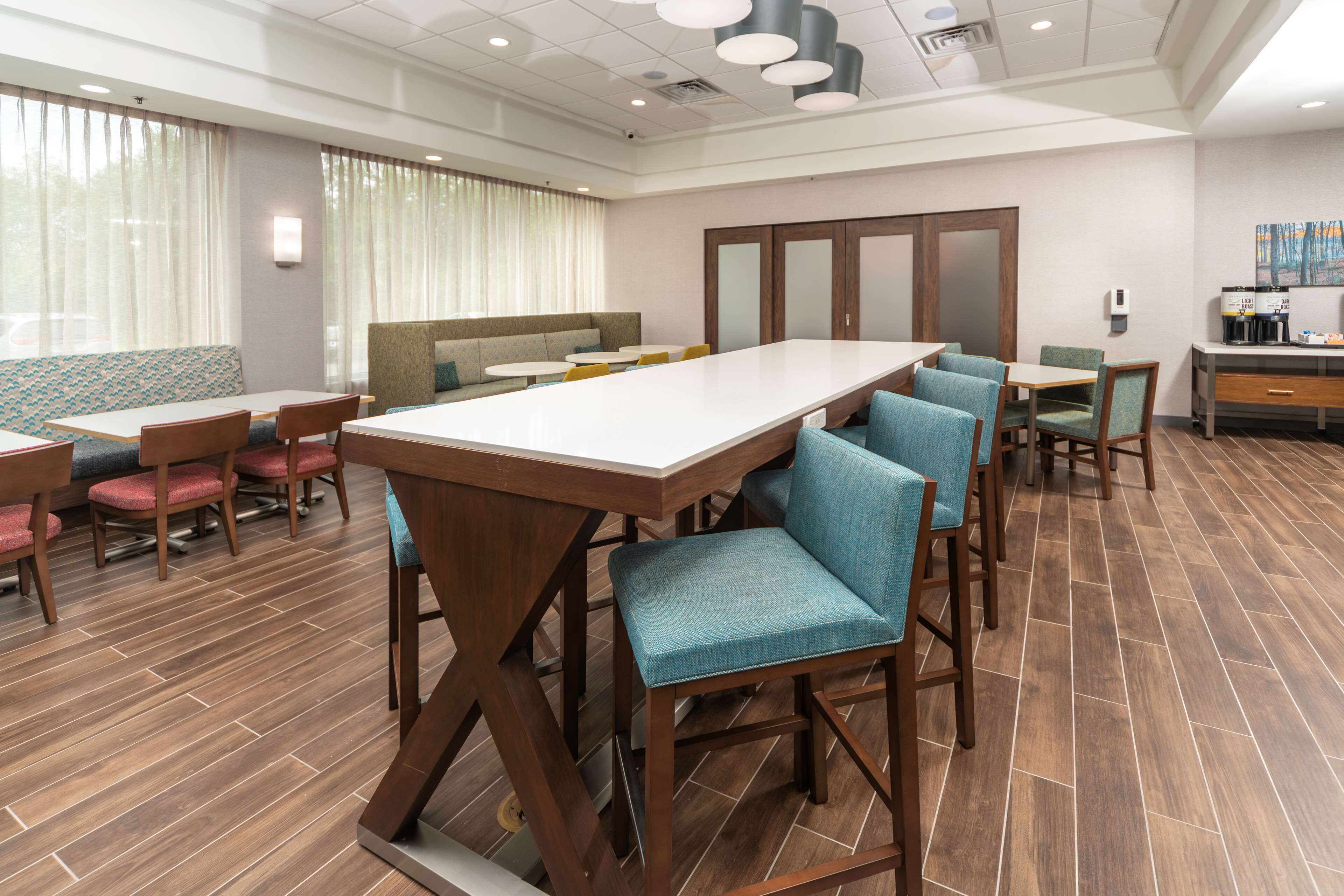 A hotel dining area with a long table, several chairs, a sofa, and a coffee station.