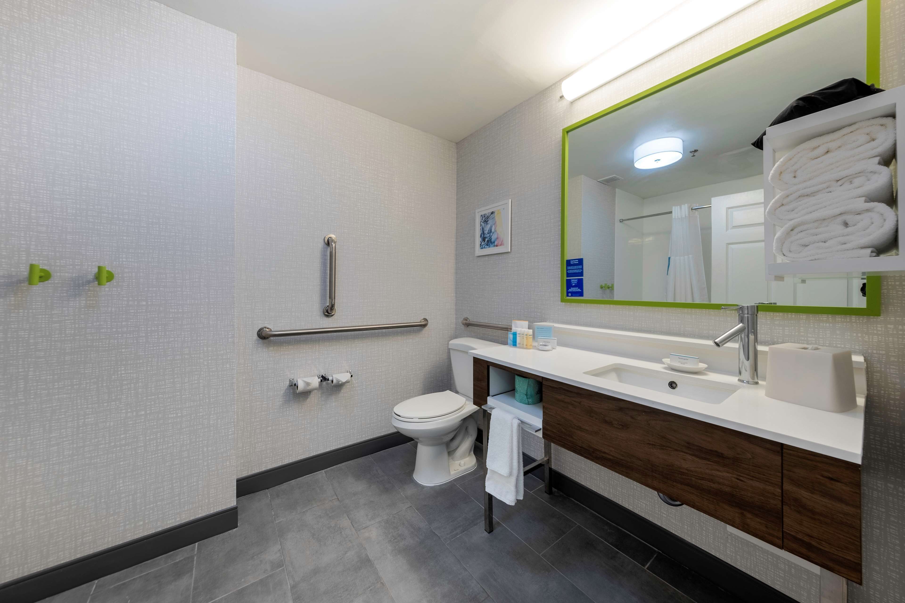 Un baño moderno con inodoro blanco, lavamanos con espejo y perchero.
