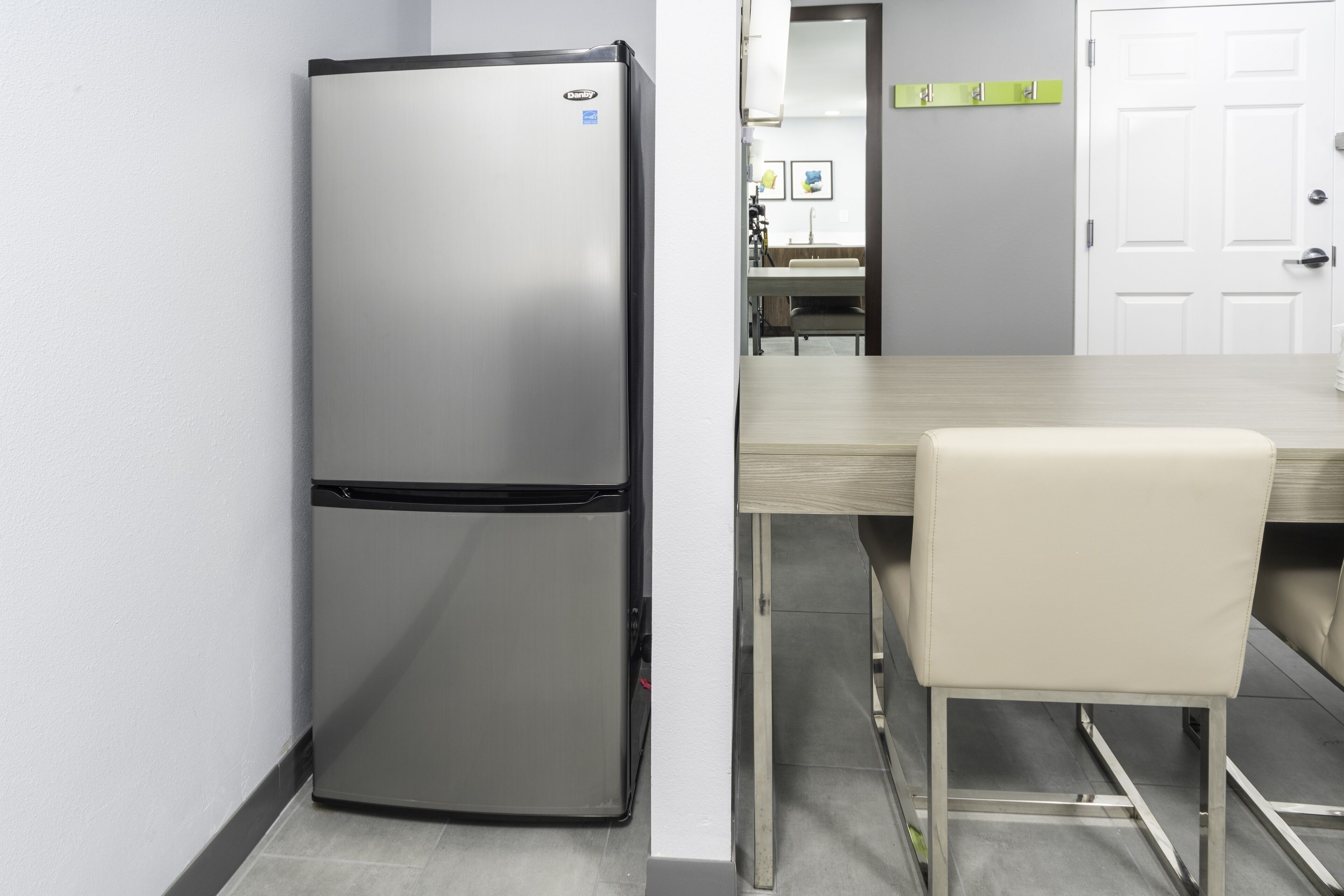 Una cocina compacta con refrigerador de acero inoxidable, una mesa de comedor de madera y una sola silla.