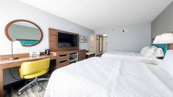 A hotel room with a bed, a desk with a chair, a TV, a mirror, and a lamp.