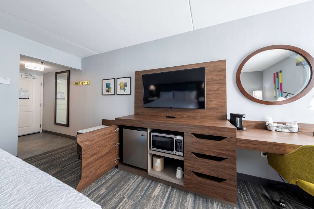 A hotel room with a wooden desk, a flat-screen TV, a microwave, a coffee maker, and a mirror.