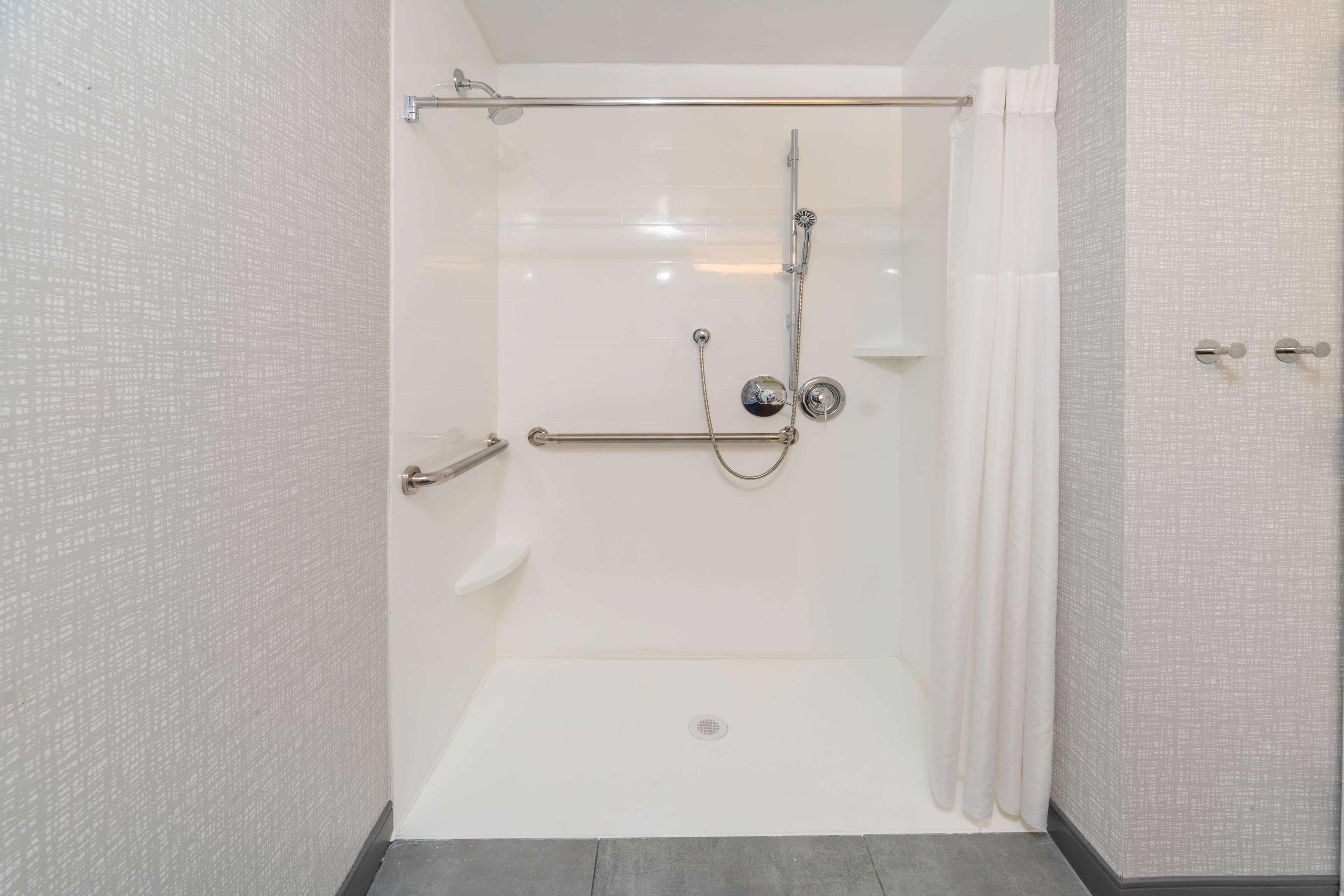Une douche à l’italienne avec une porte en verre, une barre d’appui et un pommeau de douche.
