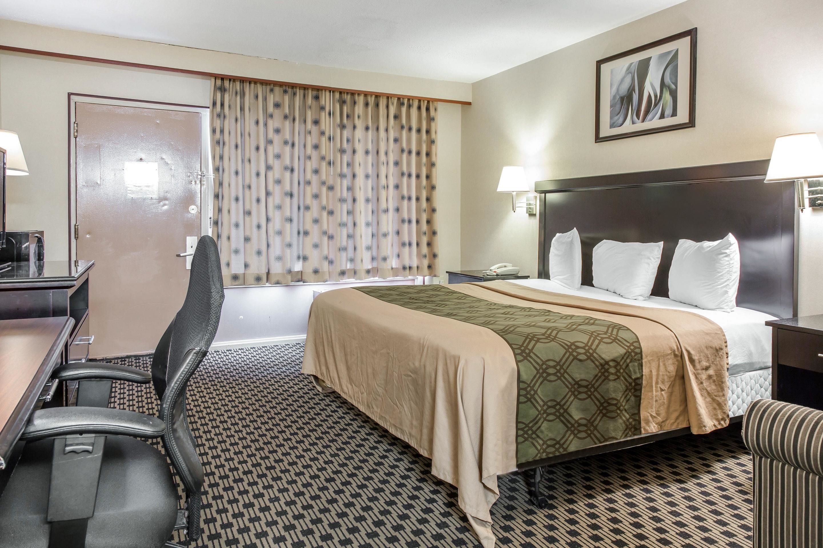 A hotel room with a bed, a desk, a chair, a telephone, and a window with curtains.