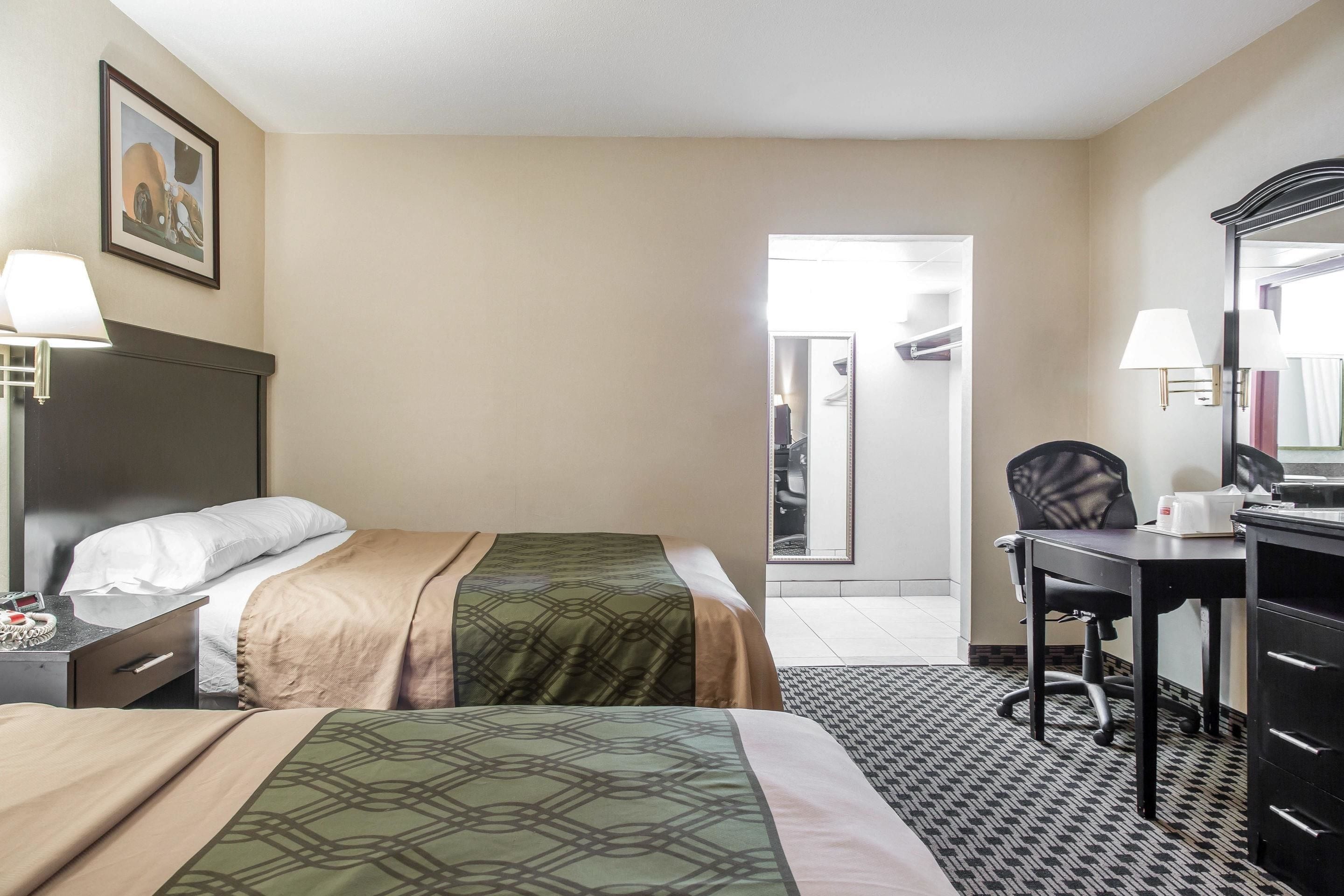 Una habitación de hotel con dos camas, un escritorio, una silla, un aparador y un espejo.