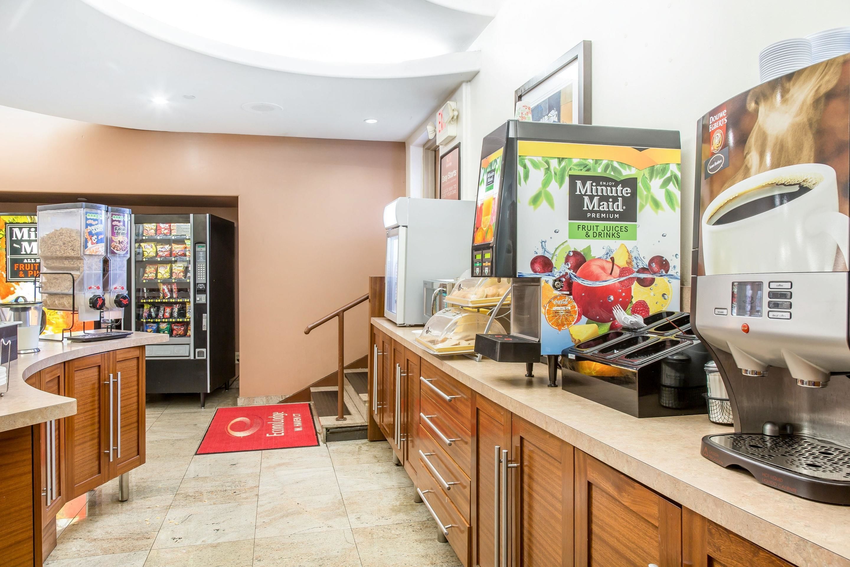 Una estación de bebidas de autoservicio con una máquina de café, un dispensador de jugo Minute Maid y un refrigerador para bebidas.
