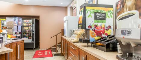 Una estación de bebidas de autoservicio con una máquina de café, un dispensador de jugo Minute Maid y un refrigerador para bebidas.