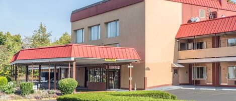 A hotel with a red roof and beige walls, featuring a registration area and a parking lot.