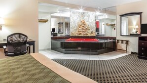 A hotel room with a large mirror, a stone wall feature, a red hot tub, and a patterned rug.
