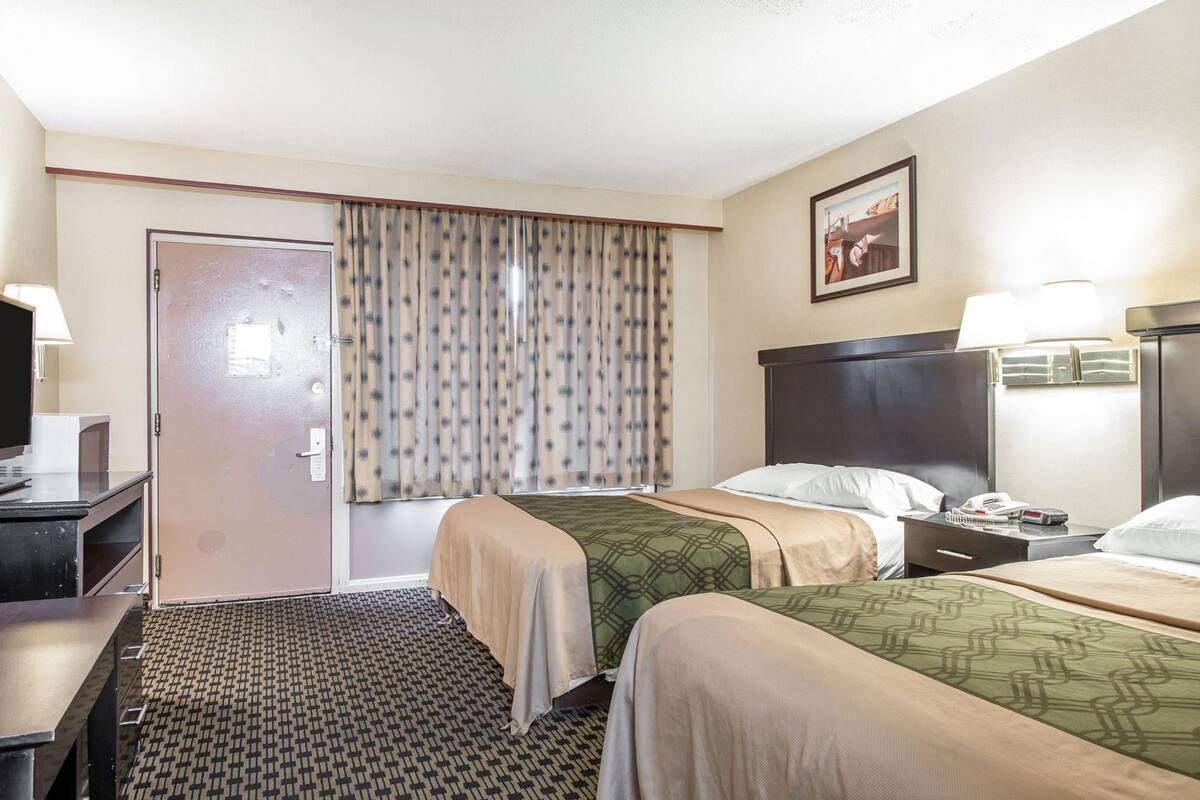 Ett hotellrum med två sängar, ett skrivbord, en stol, en TV och ett fönster med gardiner.