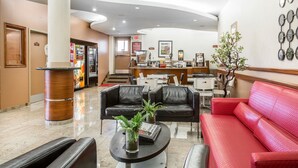 A hotel lobby with a reception desk, black leather sofas, a red sofa, a coffee machine, and a plant.
