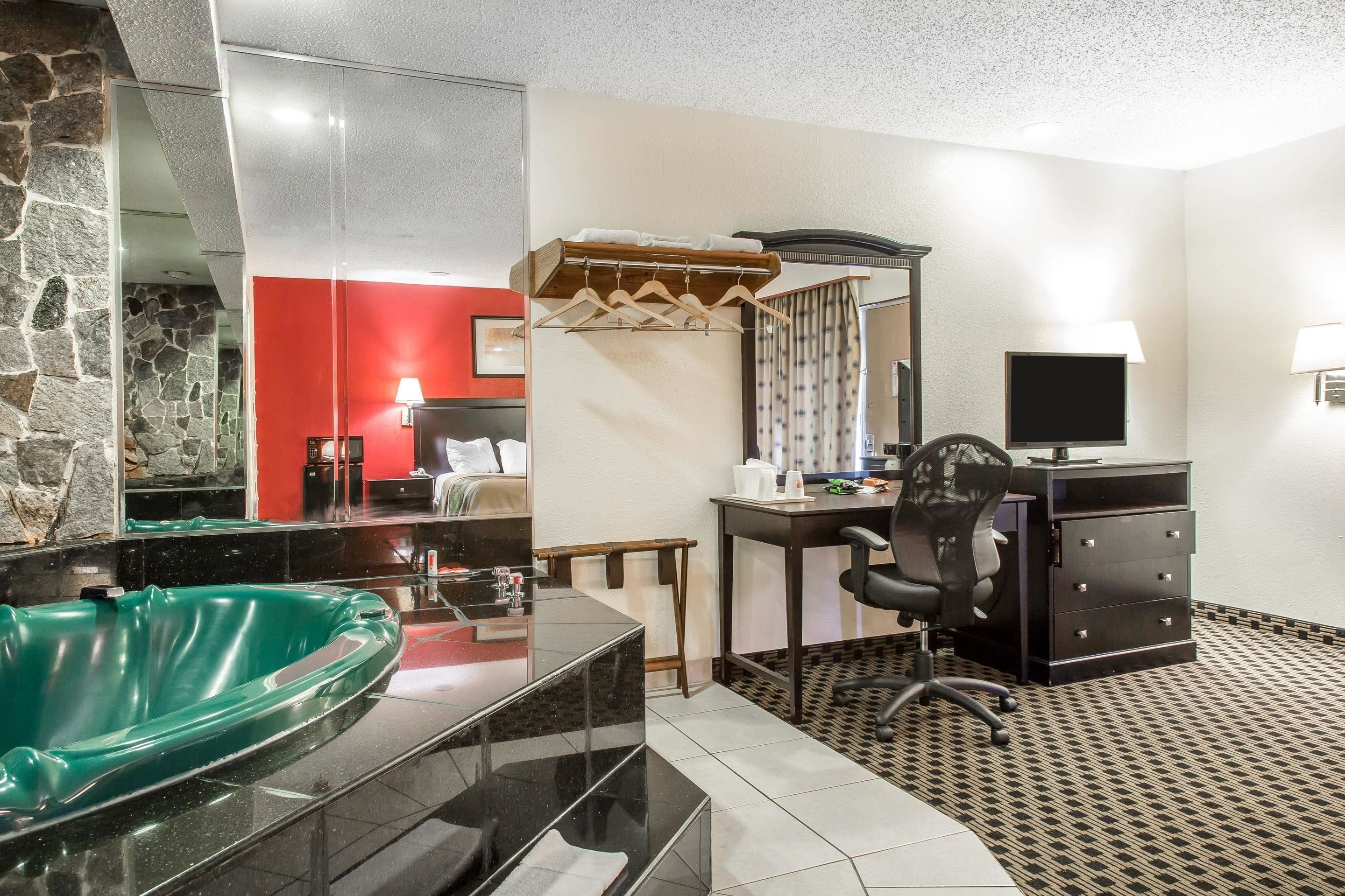 Une salle de bain avec un lavabo sur pied de couleur verte, un miroir, un étendoir à linge en bois, un bureau avec une chaise et un téléviseur.