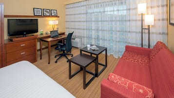 Ein Hotelzimmer mit Bett, Schreibtisch mit Computer, Fernseher, rotem Sofa und einem Fenster mit Vorhängen.