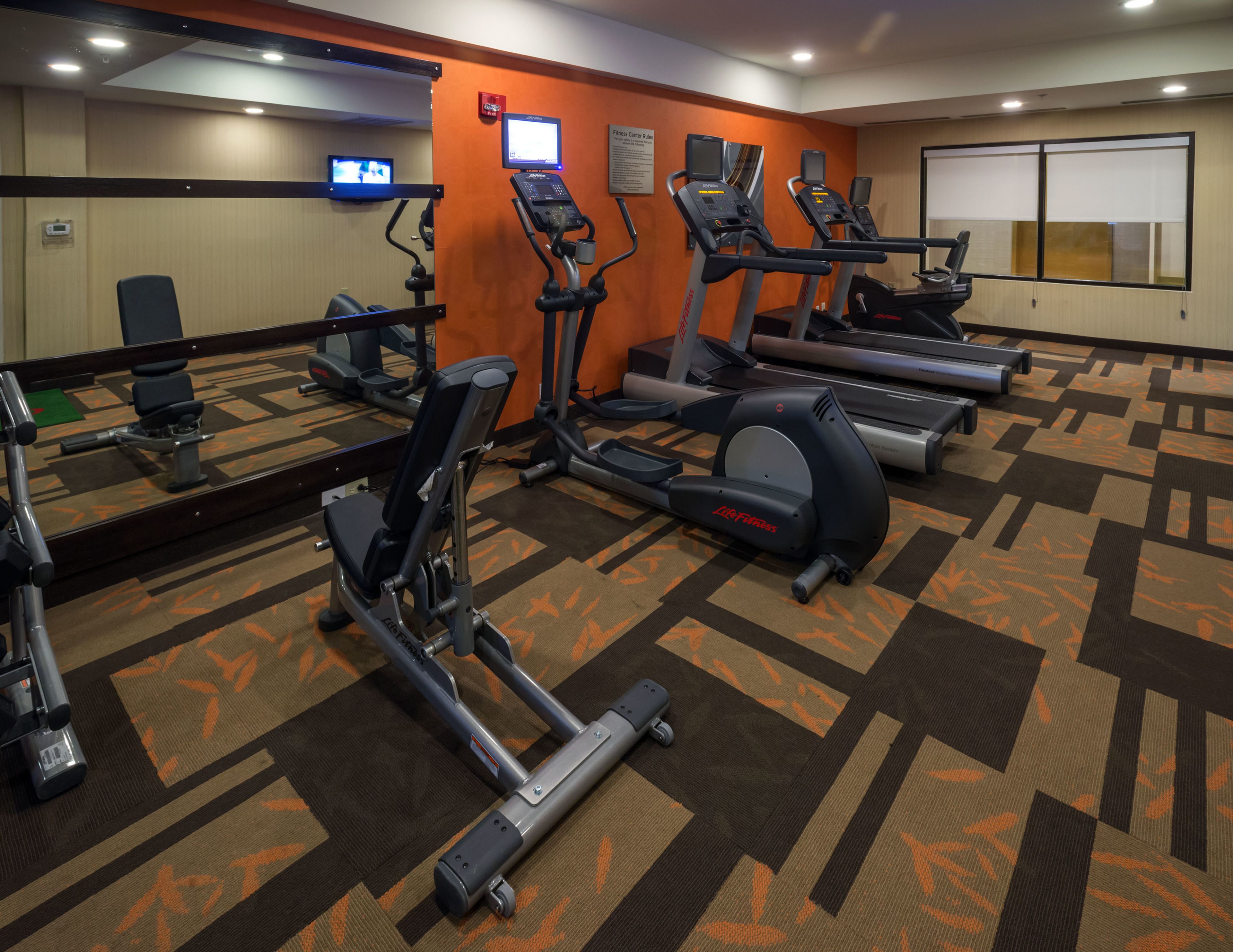 A gym with treadmills, exercise bikes, and a mirrored wall.