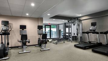 A modern gym with cardio machines, weightlifting equipment, and a mirrored wall.