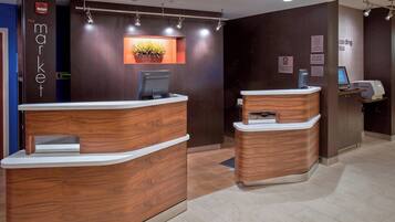 A reception area with wooden reception desks, a digital screen, and a potted plant.