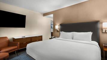 A hotel room with a large bed, a flat-screen TV mounted on the wall, a wooden dresser, a desk with a lamp, and a chair.