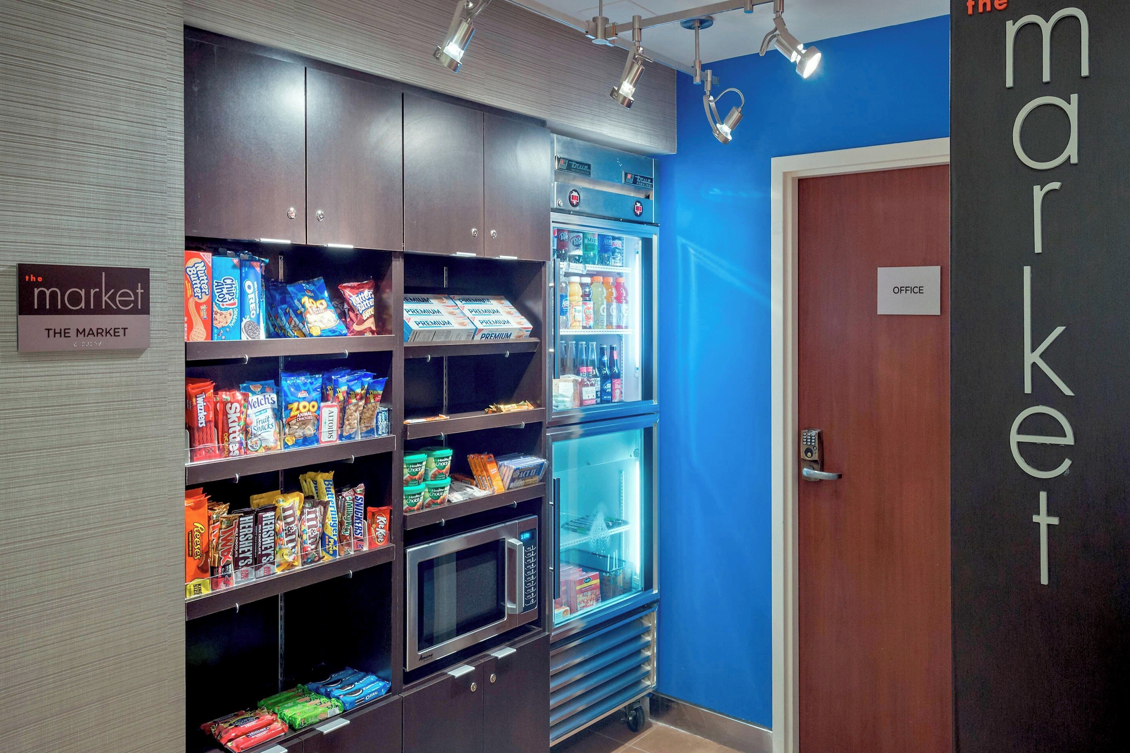 Ein Automatenbereich mit Snacks und einer Mikrowelle, eine blaue Wand und eine Tür mit der Aufschrift 'OFFICE'.