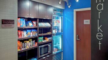 Ein Automatenbereich mit Snacks und einer Mikrowelle, eine blaue Wand und eine Tür mit der Aufschrift 'OFFICE'.