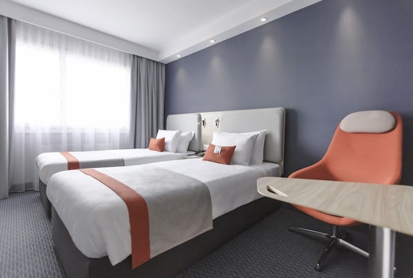 A hotel room with two beds, a desk, and a chair.