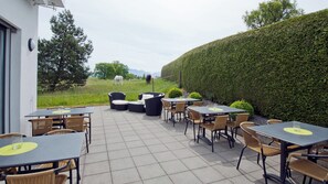 Une terrasse extérieure avec des tables et des chaises, une haie et un cheval en arrière-plan.