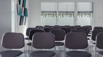 A room with rows of chairs facing a wall with a geometric pattern and a window with horizontal blinds.