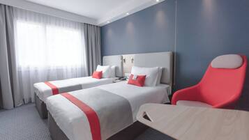 A hotel room with two beds, a desk, and a chair.