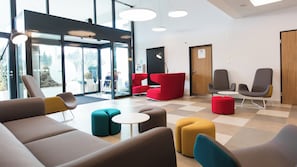 A modern lounge area with seating arrangements, a checkered floor, and a view through glass doors.