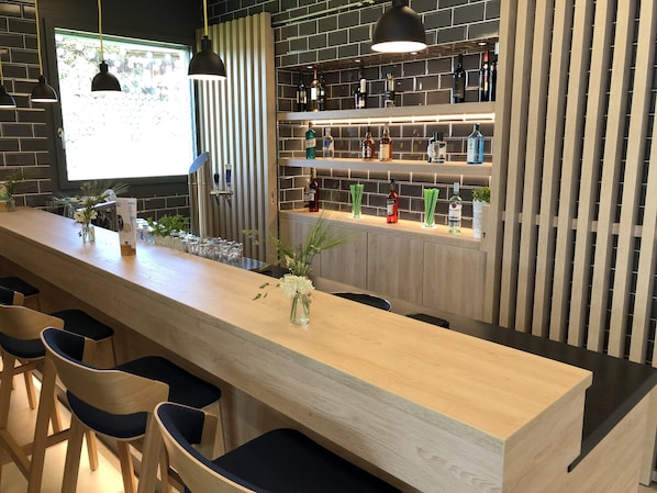 A bar area with a long counter, multiple stools, and a variety of bottles on shelves. - Holiday Inn Express Luzern - Neuenkirch by IHG (Neuenkirch)