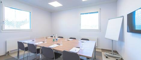A conference room with a long table, chairs, a whiteboard, and windows with blinds.