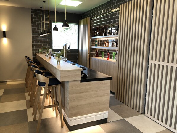 Un'area bar moderna con un lungo bancone, sgabelli da bar e una selezione di bottiglie e bicchieri.