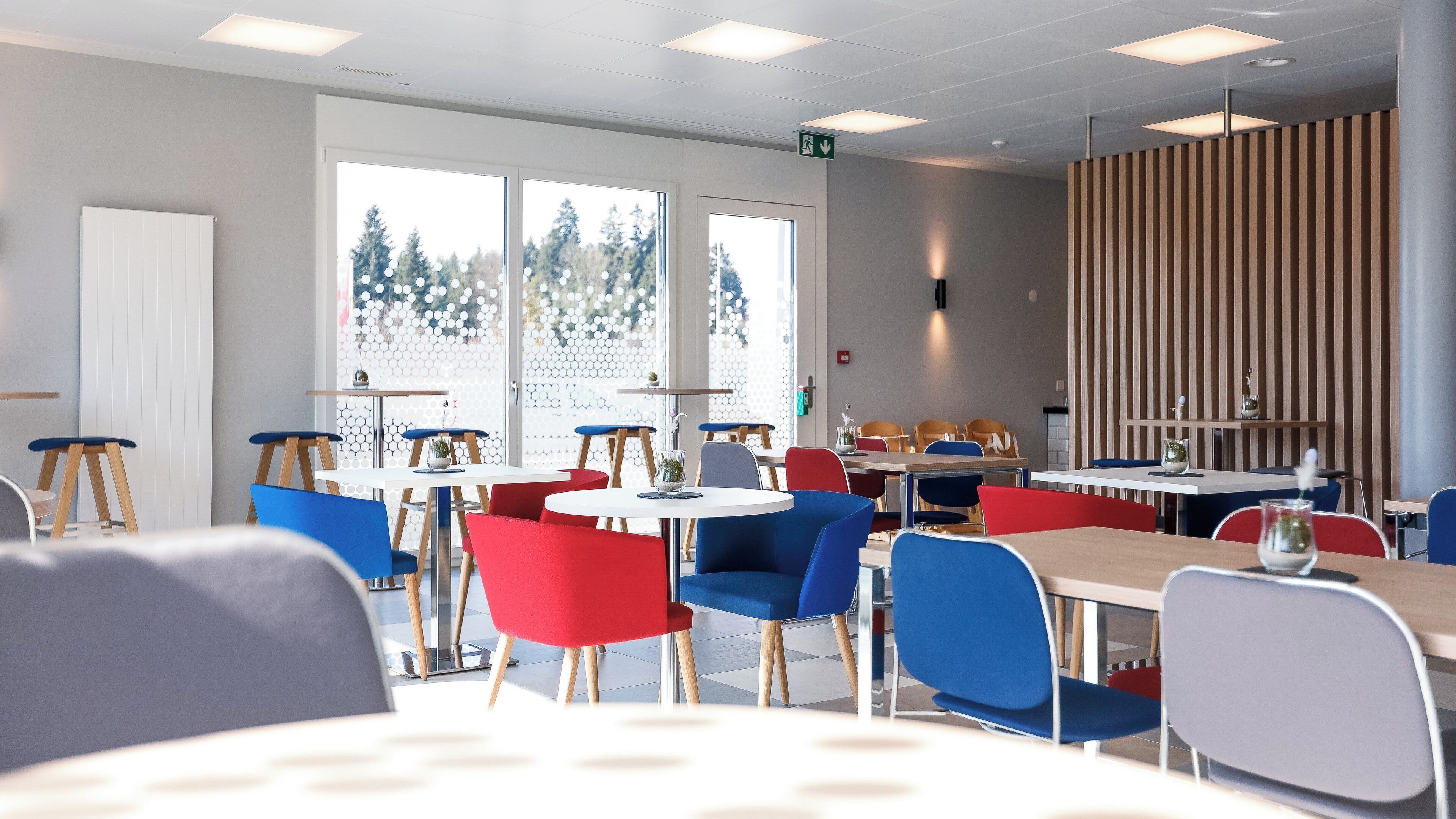 A modern dining area with tables and chairs, large windows, and a striped wall.