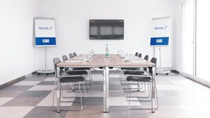Une salle de conférence avec une longue table, des chaises, une bouteille et deux panneaux d’accueil.