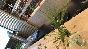 Ein modernes Interieur mit einem Holzbüroempfang, einer Vase mit weißen Blumen und Blick auf den Empfangsbereich mit einem großen Fenster und einer Treppe.