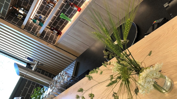 A modern interior with a wooden reception desk, a vase with white flowers, and a view of the lobby area with a large window and a staircase. - Holiday Inn Express Luzern - Neuenkirch by IHG (Neuenkirch)