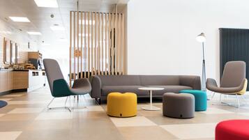 Un espacio de oficina moderno con un sofá gris, sillas verde azulado y amarillas, y un otoman rojo.