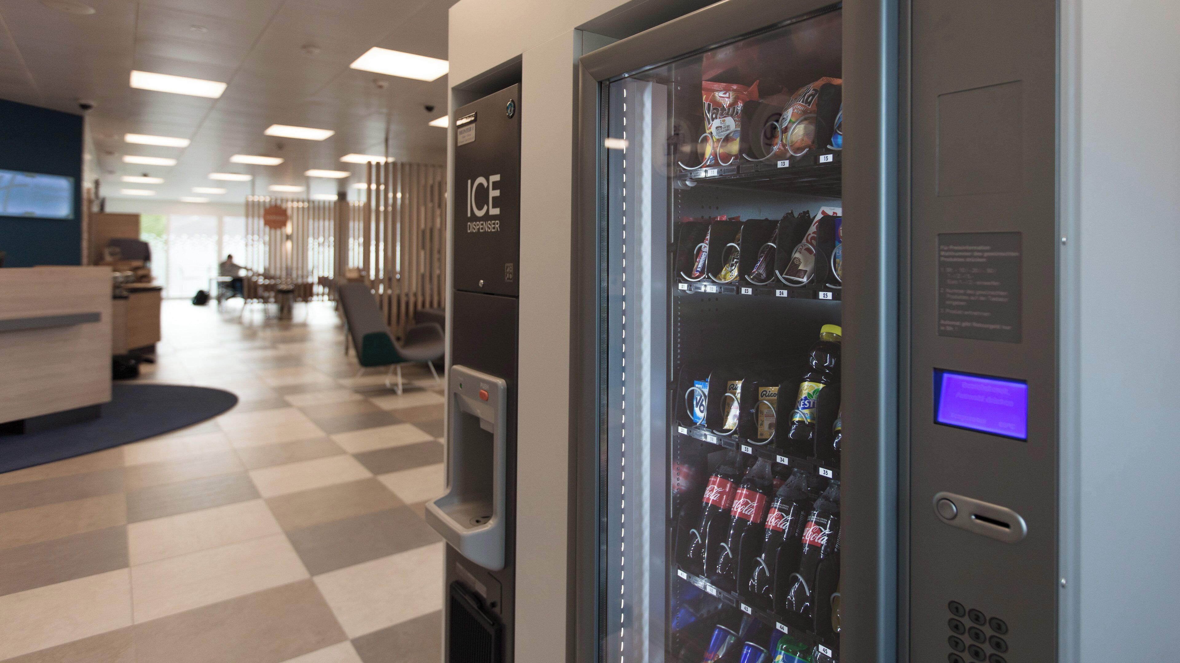A vending machine with various beverages and a CE dispenser in a modern office setting.