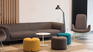 A modern living room with a sofa, ottomans, a small round table, a floor lamp, and a chair. - Holiday Inn Express Luzern - Neuenkirch by IHG (Neuenkirch)