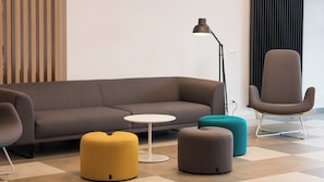 A modern living room with a sofa, ottomans, a small round table, a floor lamp, and a chair. - Holiday Inn Express Luzern - Neuenkirch by IHG (Neuenkirch)
