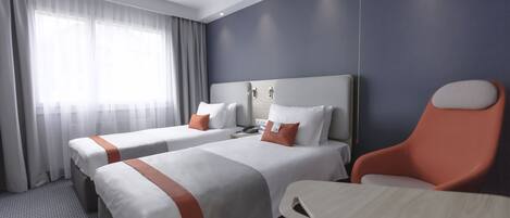 A hotel room with two beds, a desk, and a chair.