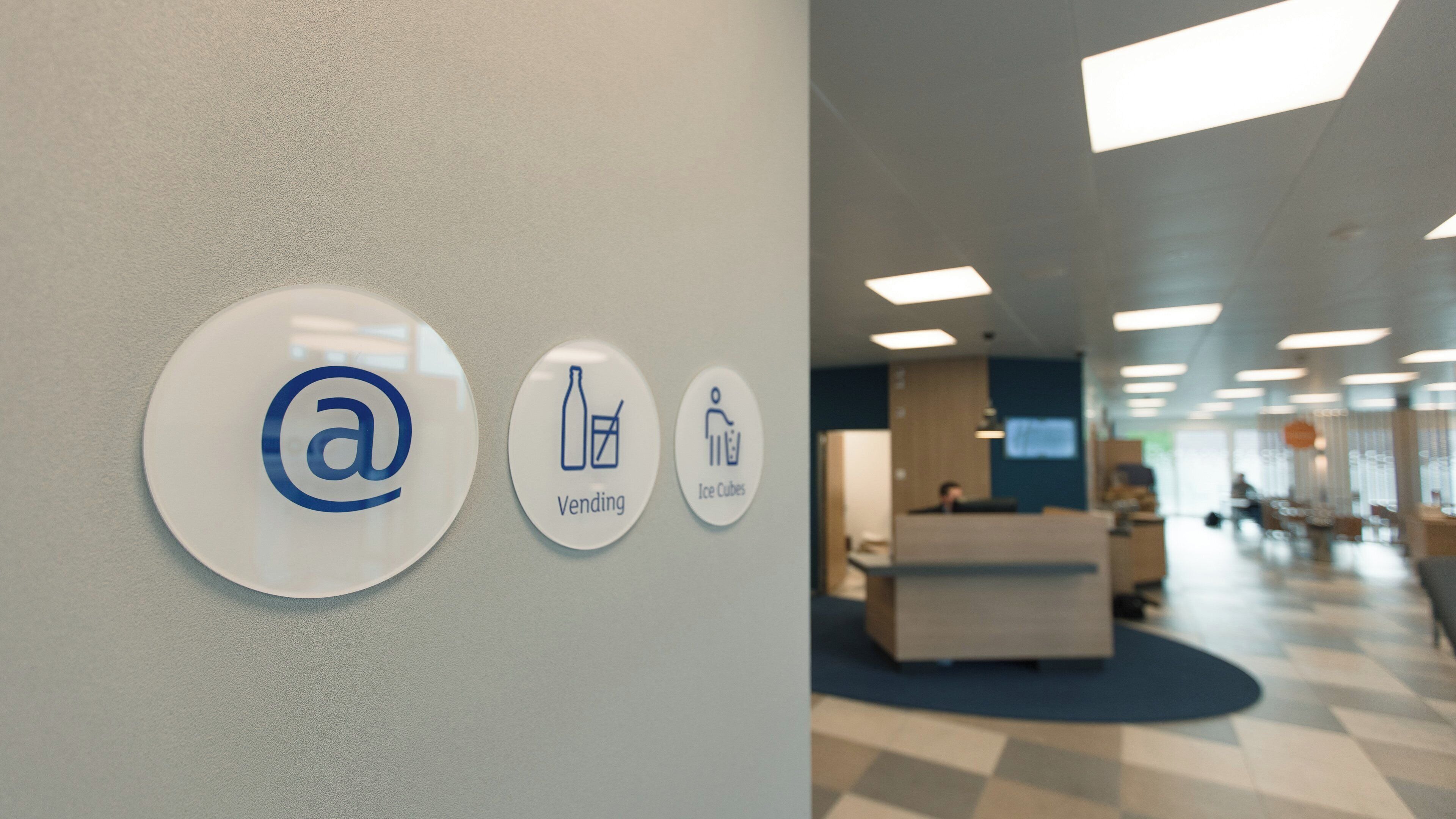 Zona de recepción con mostrador y pared que muestra tres señales circulares con iconos para correo electrónico, máquinas expendedoras y hielo.