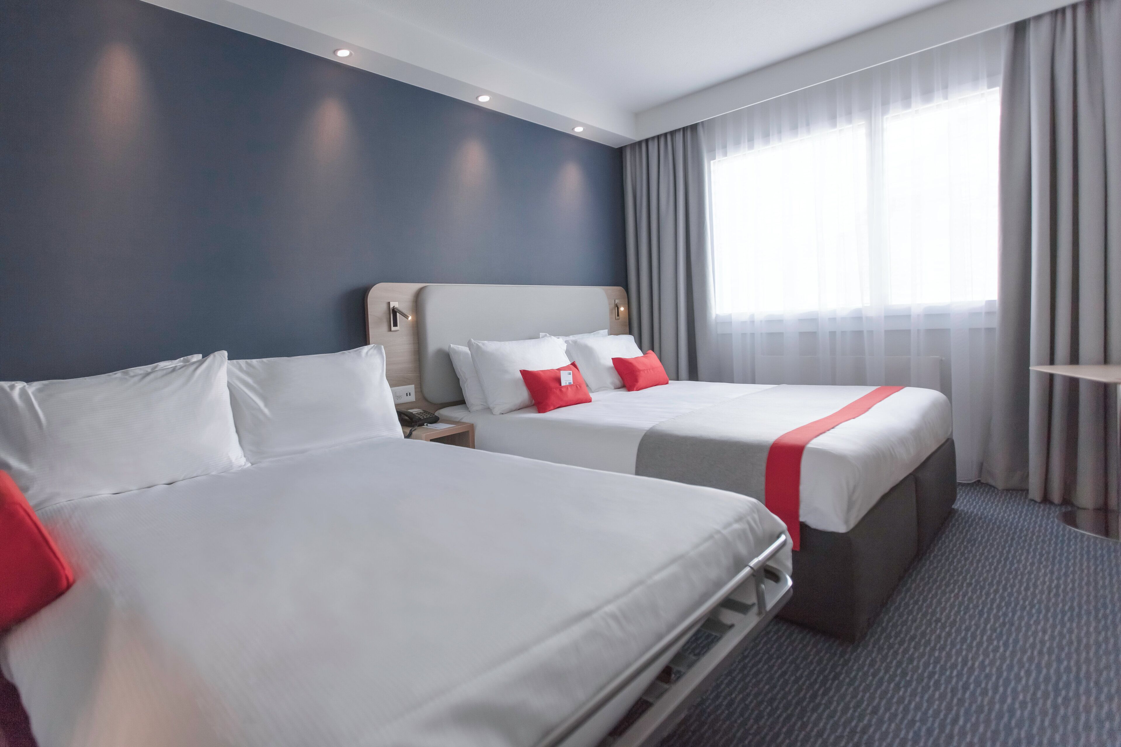 A hotel room with two beds, a nightstand, a telephone, and a window with curtains.
