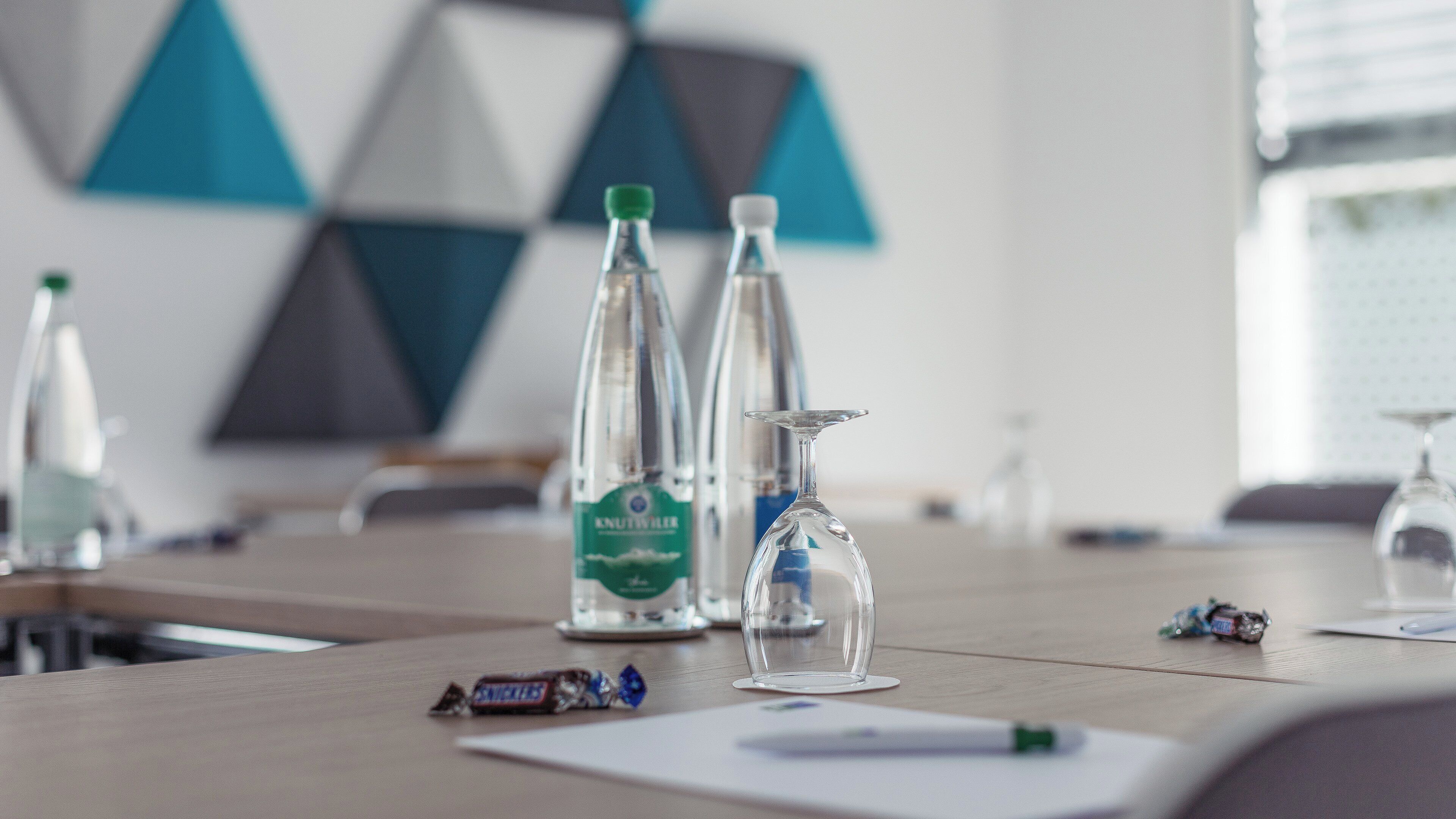 A conference table with water bottles, a glass, and a Snickers bar.