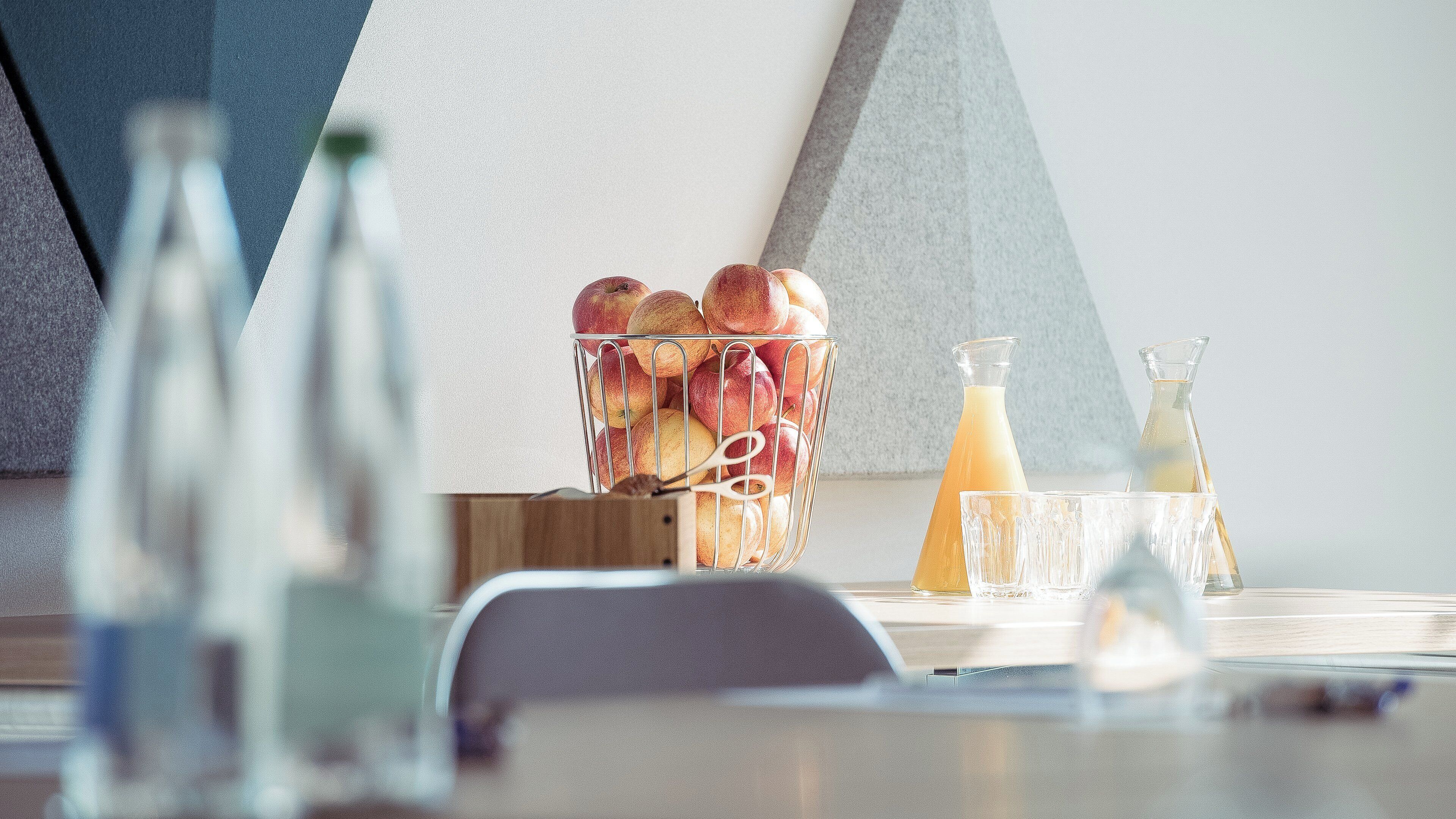 Een keukentafel met een fruitmand, een glazen karaf en een waterkan.